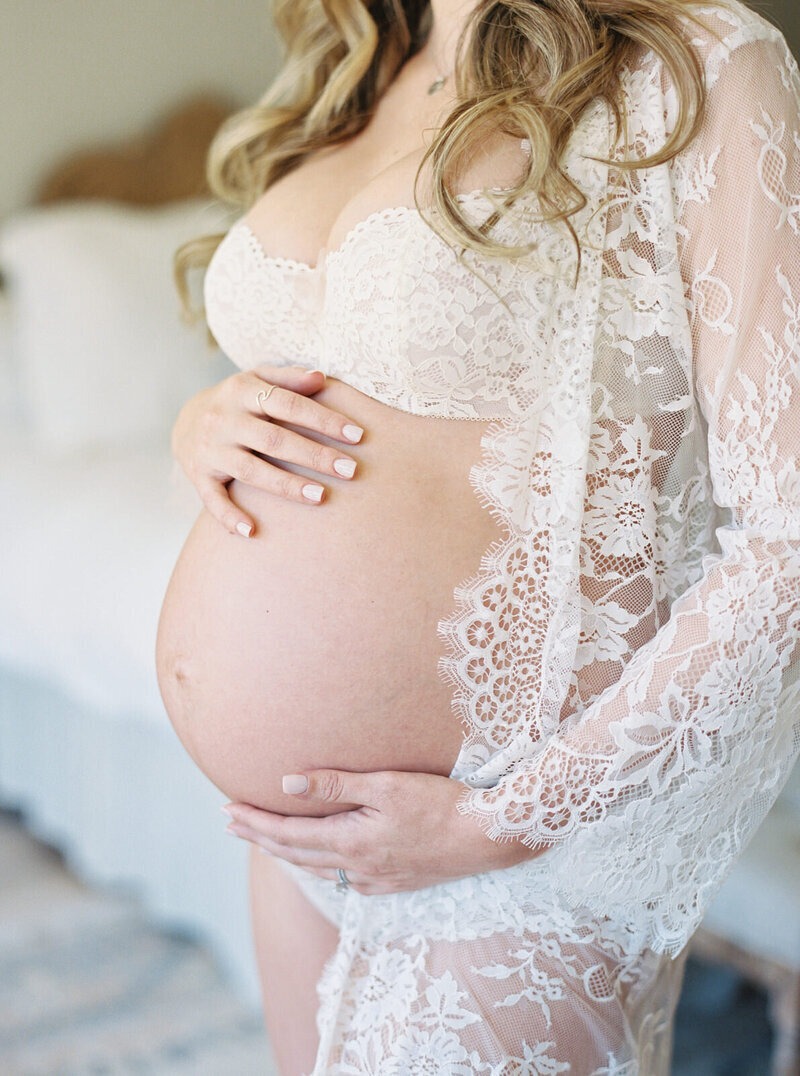 closeup of a woman in white, with her hands on her pregnant belly, looking beuatiful after she followed maternity photo session tips